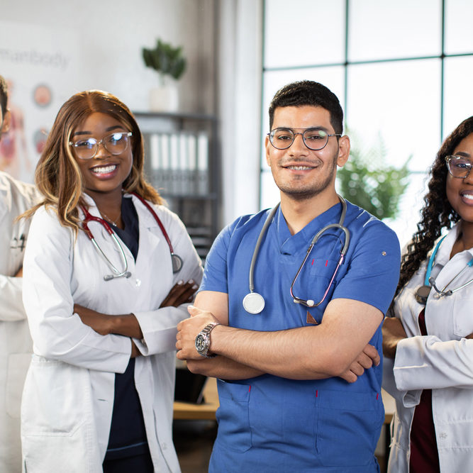 beautiful medical nurse and colleagues in hospital Portrait of smiling multiethnic medical team standing in modern clinic room with arms crossed. Group of pleasant confident skilled multiracial physicians posing indoors with arms folded