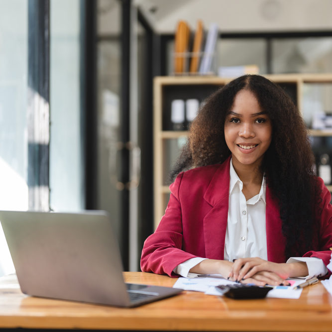 Black Businesswoman Sitting at Her Desk Working on a Laptop Computer. Smiling Successful African American Woman working with Big Data e-Commerce Black Businesswoman Sitting at Her Desk Working on a Laptop Computer. Smiling Successful African American Woman working with Big Data e-Commerce.